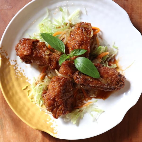 Crispy fried chicken wings with sauce, shredded lettuce, carrots, and basil on a white plate.