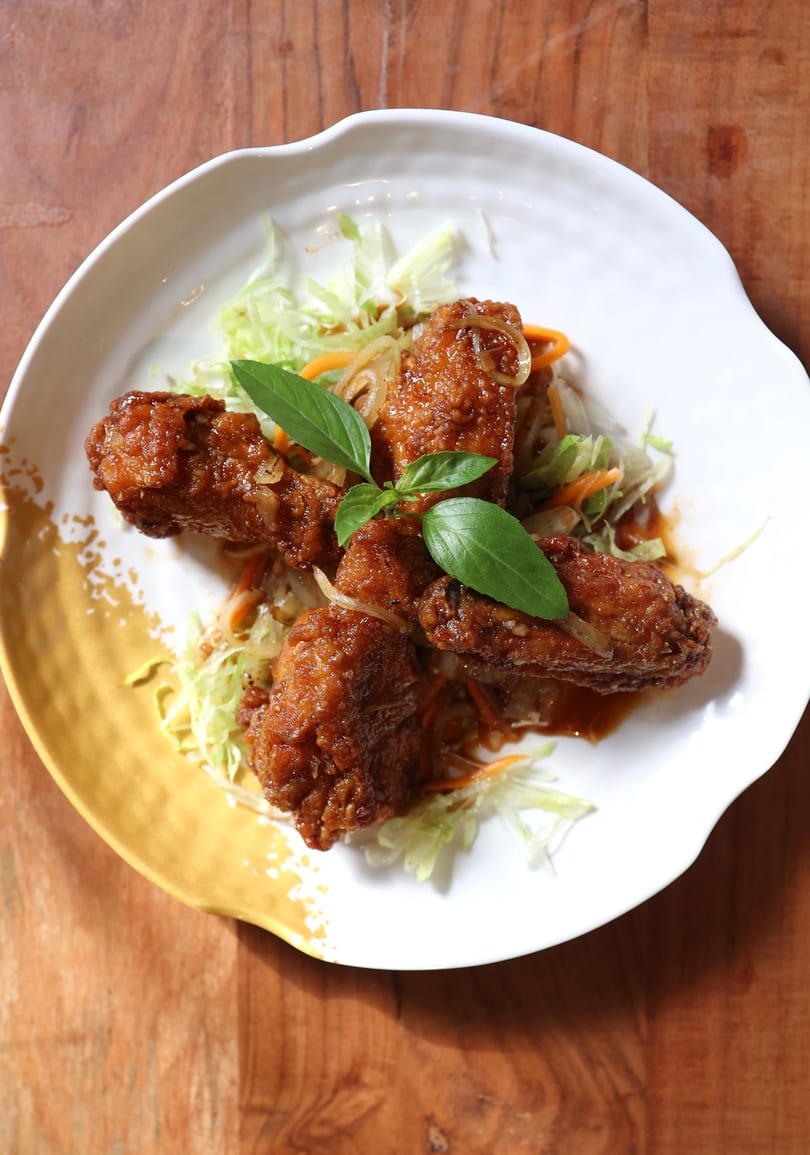 Crispy fried chicken wings with sauce, shredded lettuce, carrots, and basil on a white plate.