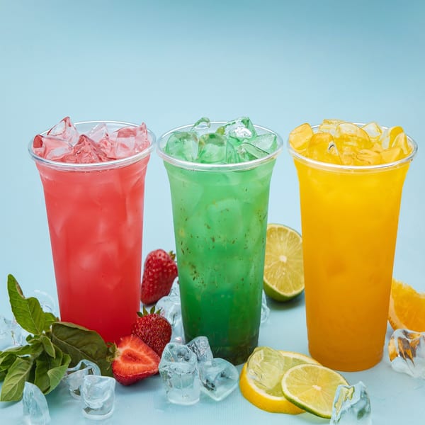Three colorful iced drinks, red, green, and yellow, with fresh fruit and ice on a blue background.